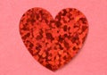 Red flat shiny foil heart on pink tectured paper background close up