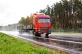 A red flatbed semitrailer tractor driving on the road in rain and poor visibility in summer. Poor visibility concept in Royalty Free Stock Photo