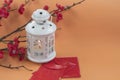 White lantern light with red flowers branch and red envelopes on orange background.