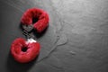 Red fluffy handcuffs on black textured surface. Space for text Royalty Free Stock Photo