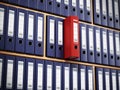 Red folder standing out among black ones inside wooden shelves. 3D illustration Royalty Free Stock Photo