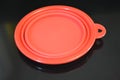 Red folding and multifunctional rubber plate, a bowl with a plastic edging on a black glossy surface.