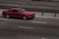 Red ford mustang rides on the road. Against a background of blurred trees