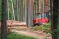 Red forest machine that clears trees in green summer forest standing near sandy road surrounded by growing tree trunks Royalty Free Stock Photo