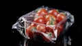 Red fresh cherry tomatoes in a plastic box wrapped in oilcloth transparently rotating on a black background