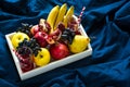 Red fresh juice with apples, pears, bananas, grapes and pomegranate fruits in white wooden tray on blue bed shee Royalty Free Stock Photo