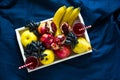 Red fresh juice with apples, pears, bananas, grapes and pomegranate fruits in white wooden tray on blue bed shee Royalty Free Stock Photo