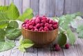 Red fresh raspberries on brown rustic wood background. Bowl with natural ripe organic berries with peduncles, green leaves Royalty Free Stock Photo