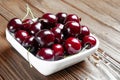 Red fresh ripe juicy sweet cherries in a white plate on a wooden background. Wet sweet cherries with water drops Royalty Free Stock Photo