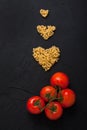 Red fresh tomatoes and pasta heart shape black concrete background. Royalty Free Stock Photo