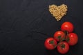 Red fresh tomatoes and pasta heart shape black concrete background. Royalty Free Stock Photo