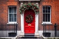 Red front door with Christmas wreath and street festive decorations on holidays. Generated by AI Royalty Free Stock Photo