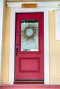 Red front door of home with glass pannel and white frame with beige paint on front porch with sign on top and red steps Royalty Free Stock Photo