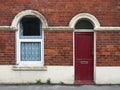 Red front door and window of a typical old brick british terraced house with shabby peeling paintwork Royalty Free Stock Photo
