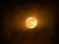 Red full super moon glowing against clouds in a dark sky