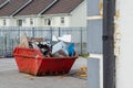Red garbage removal skip full of rubbish and ready for collection in a street. Old dumpster full of junk in a yard. Waste industry Royalty Free Stock Photo