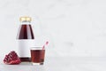 Red garnet juice in glass bottle mock up with blank label, straw, wine glass, fruit slice on white wood table in light interior.