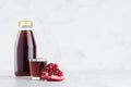 Red garnet juice in glass bottle mock up with wine glass, fruit slice on white wood table in light interior, template.