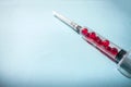 Red gel capsules inside a syringe with a needle on a blue background. Medicines, vaccination. Opioid epidemic, drug abuse and Royalty Free Stock Photo