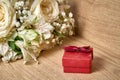 Red gift box with bow on lid, bouquet of white flowers on wooden background, holiday