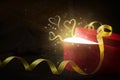 Red gift box on a dark background with ribbon, magic light, gold dust, bokeh and glowing hearts above it. Copy space Royalty Free Stock Photo