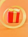 Red Gift box at the end of the spiral yellow ribbon, orange background, vertical. Royalty Free Stock Photo
