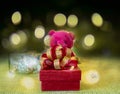 A red gift box with golden ribbon in a pink Teddy bear arms standing on green fabric, a glass bottle in the back bokeh Royalty Free Stock Photo