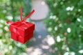 Red gift box on green nature background with copy space, surprise for birthday or valentine`s day