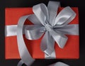 Red gift box with grey ribbon and bow on black background