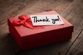 Red gift box and label with the words thank you on a wooden background: concept of expressing gratitude and thanks