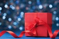 Red gift box or present with bow ribbon against blue bokeh background. Christmas greeting card. Royalty Free Stock Photo