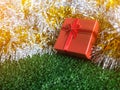 Red gift box with red ribbon bow and golden seam place on silver and gold rainbow glowing decoration background on green grass. Royalty Free Stock Photo