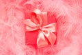 Red gift box with satin bow on pastel pink background made of feathers. Festive boho style concept Royalty Free Stock Photo