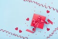 Red gift box, serpentine, hearts and confetti on blue background top view. Valentine`s day greeting card. Flat lay. Royalty Free Stock Photo