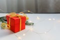 Red gift box tied with gold ribbon on a light table with bokeh lights and blurred background Royalty Free Stock Photo