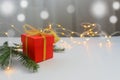 Red gift box tied with gold ribbon on a light table with bokeh lights and blurred background Royalty Free Stock Photo