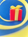 Red Gift box at the end of the spiral yellow ribbon, blue background. Vertical. Royalty Free Stock Photo