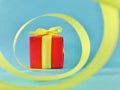 Red Gift box at the end of the spiral yellow ribbon, teal background. Royalty Free Stock Photo