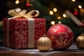 a red gift box and two ornaments on a table with a christmas tree in the background Royalty Free Stock Photo