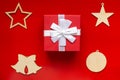 Red gift box with white bow and Christmas wooden decorations in the form of stars, bells and ball, on a red background Royalty Free Stock Photo