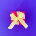 Red gift box with yellow ribbon on purple background . square. Royalty Free Stock Photo