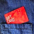 A red gift card comes out of a blue denim pocket. close up view.