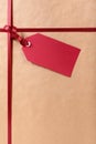 Red gift tag and ribbon, brown wrapping paper background, vertical, copy space Royalty Free Stock Photo