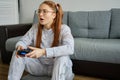 Red girl with tails in glasses sits on the floor and enthusiastically plays joystick.