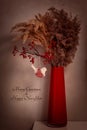 A red glass vase stands on a shelf against a dark wall. In vase are dried grass, spikelets, dried flowers, red berries. Royalty Free Stock Photo