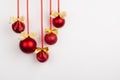 Red glossy christmas balls with gold shimmer bows hang on ribbon on white wall, copy space. Christmas background for design. Royalty Free Stock Photo