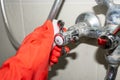 A red-gloved hand rubs a hot water knob on a chrome-plated faucet covered with limestone with a white melamine sponge