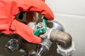 A red-gloved hand turns a green knob on a connecting valve on a chrome-plated faucet, covered with limestone