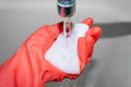 Red gloved hand wets white melamine sponge under tap water in bathroom