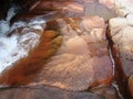 Red granite stones by flowing water of waterfall over it. Royalty Free Stock Photo